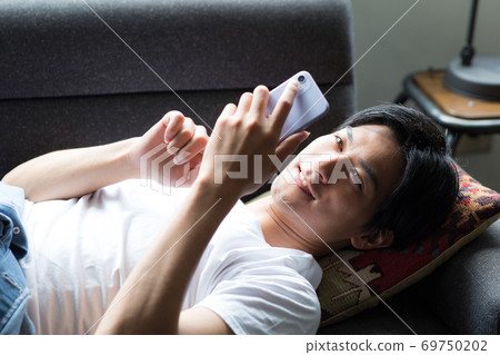 A man lying on the sofa and looking at his smartphone 69750202