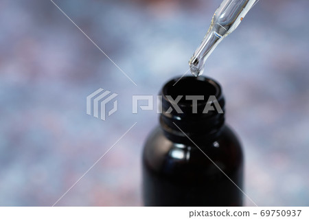 Drop falls from a pipette into a cosmetic bottle Drop falls from a pipette into a cosmetic bottle 69750937