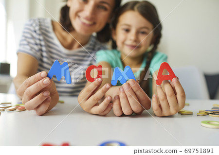 Happy mother and preschool daughter playing with set of wooden letters and making word Mama 69751891