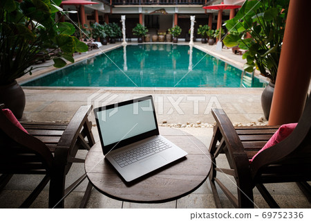 A white laptop on wooden table swiming pool background. 69752336