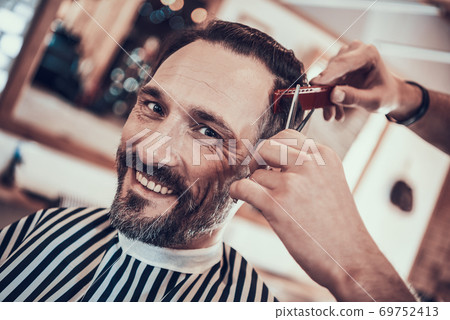 Man smiles as he gets hair cut in a barbershop. 69752413