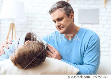Dad reassures son who offended and lies on pillow. Dad reassures son who offended and lies on pillow. 69753070