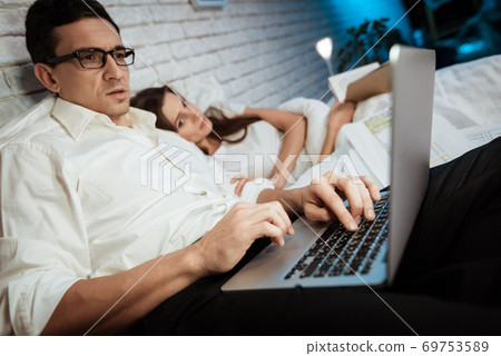 A man with glasses lies in bed and works at laptop A man with glasses lies in bed and works at laptop 69753589