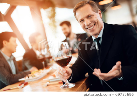 A man in a suit with a glass of wine in his hand. 69753696