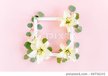 Floral frame made of white lilies and eucalyptus leaves on pink background. Flat lay, top view floral mockup with empty space for text. Floral pattern 69756241
