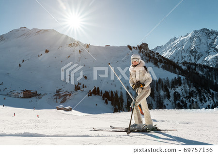 Young adult beautiful happy attractive caucasian smiling skier woman full lenght body portrait mountain peak showing skiing resort panorama breathtaking view. Winter travel adventure welcome concept 69757136