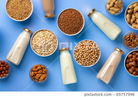 Bottles of vegan non dairy milk with various nuts on blue background 69757996