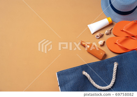 Beach bag with suntan products, flip-flops and hat on beige background 69758082