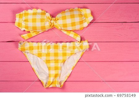 Yellow bikini on bright pink wooden background Yellow bikini on bright pink wooden background 69758149