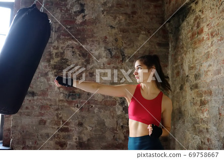 Young woman hits punching bag during a boxing training. Female boxer doing fitness. Young woman hits punching bag during a boxing training. Female boxer doing fitness. 69758667