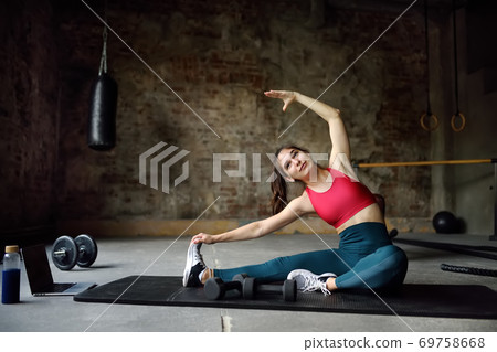 Girl stretching or yoga in gym using a laptop with online training. Girl stretching or yoga in gym using a laptop with online training. 69758668