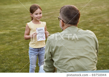 I love you daddy. Father and his cute little daughter celebrating Happy Fathers Day in park on a warm day, small girl giving her father handmade postcard and smiling 69758944