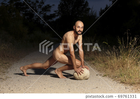 Young male athlete fully naked crouching on a trail at night looking at camera Young male athlete fully naked crouching on a trail at night looking at camera 69761331