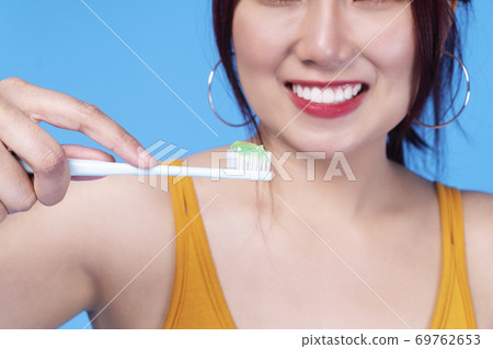 Hands of smile young woman holding toothbrush with toothpaste over isolated blue background.  69762653