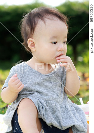 1 year old child eating a snack in the park 69763530