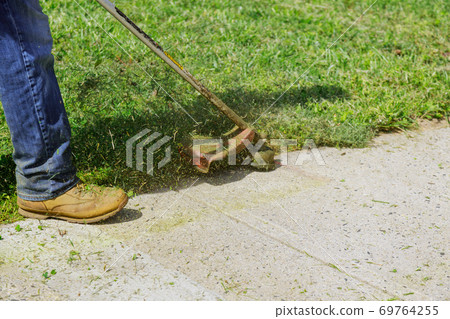 Closeup man hand using lawn trimmer mower cutting grass on green selective focus at hand Closeup man hand using lawn trimmer mower cutting grass on green selective focus at hand 69764255