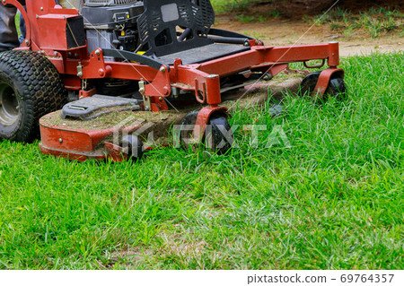 Man worker cutting grass in summer with a lawn mower Man worker cutting grass in summer with a lawn mower 69764357
