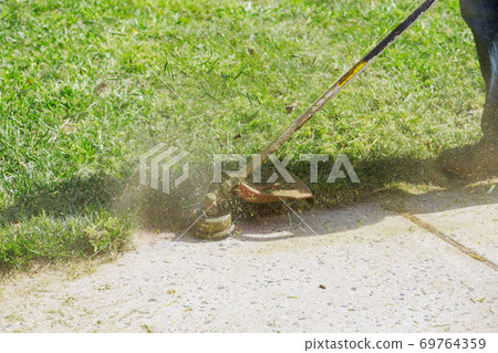 A municipal worker in an lawn mower mows fresh, green grass on the lawn near residential building. A municipal worker in an lawn mower mows fresh, green grass on the lawn near residential building. 69764359