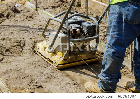 Worker use vibratory plate compactor under construction on new pavement 69764394