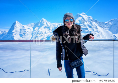 Young Woman Tourist at the Schilthorn in Switzerland with panoramic view of the Swiss Skyline. Young Woman Tourist at the Schilthorn in Switzerland with panoramic view of the Swiss Skyline. 69764680