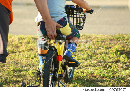 A 3-year-old boy having his mother push a bicycle A 3-year-old boy having his mother push a bicycle 69765071
