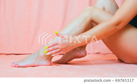 The young woman with perfect body applying refreshing cream body lotion on her legs ion a white The young woman with perfect body applying refreshing cream body lotion on her legs ion a white 69765317