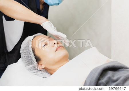 Professional cosmetician using oil pipette apply serum on clients face. 69766647