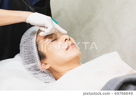 Professional cosmetician using oil pipette apply serum on clients face. 69766649