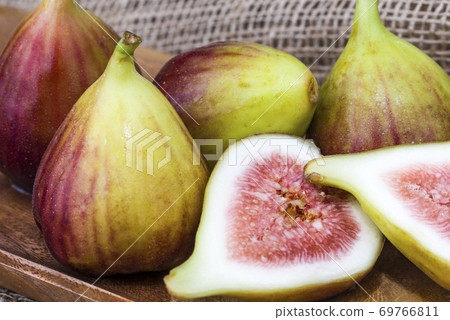 Fresh fig sliced in half with whole figs in the background, on a wooden surface. Fresh fig sliced in half with whole figs in the background, on a wooden surface. 69766811