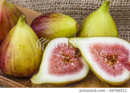 Fresh fig sliced in half with whole figs in the background, on a wooden surface. Fresh fig sliced in half with whole figs in the background, on a wooden surface. 69766812