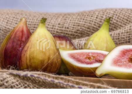 Fresh fig sliced in half with whole figs in the background, on a wooden surface. Fresh fig sliced in half with whole figs in the background, on a wooden surface. 69766813