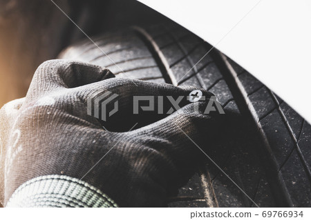 The mechanic pulled the metal screw punctured from the car tire The mechanic pulled the metal screw punctured from the car tire 69766934