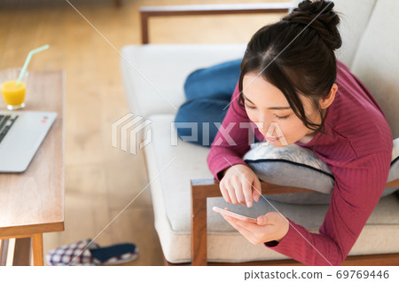 一個女人躺在沙發上，在遠程辦公期間操作智能手機 69769446