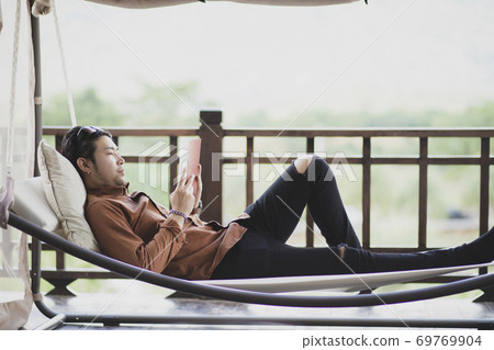 younger man relaxing by reading book on cradle 69769904