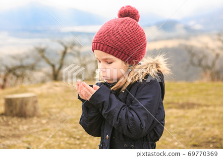 a little girl blows on her hands to warm them.  69770369