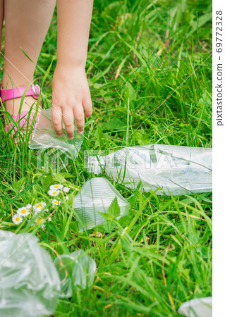 Hand of child cleans green grass from plastic trash Hand of child cleans green grass from plastic trash 69772328