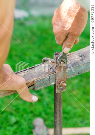 Elderly man twists the nut by wrench 69772355