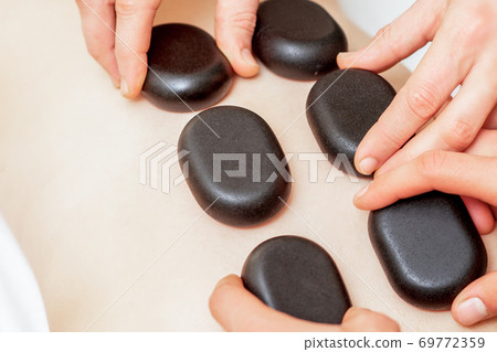 Male four hands laying stones on female back Male four hands laying stones on female back 69772359