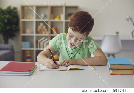Smiling little schoolboy doing homework sitting at a desk in his bright room. Smiling little schoolboy doing homework sitting at a desk in his bright room. 69774103