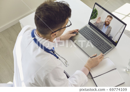 Man doctor looking at laptop screen at greeting him man patient during online consultation Man doctor looking at laptop screen at greeting him man patient during online consultation 69774109