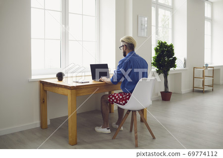 Online work at home. A young man in typing in a laptop sitting at a table at home. Remote work. Online work at home. A young man in typing in a laptop sitting at a table at home. Remote work. 69774112