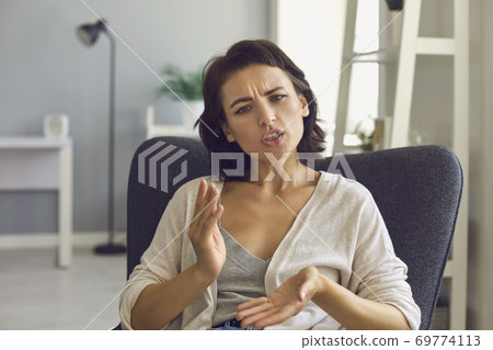 Young woman looking at web camera and explaining something with hands during online meeting Young woman looking at web camera and explaining something with hands during online meeting 69774113