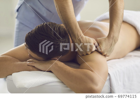 Young man getting professional remedial body massage in massage room or health center Young man getting professional remedial body massage in massage room or health center 69774115