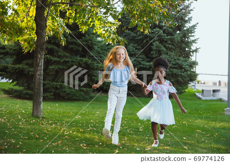 Interracial kids, friends, girls playing together at the park in summer day Interracial kids, friends, girls playing together at the park in summer day 69774126