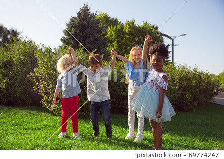 Interracial group of kids, girls and boys playing together at the park in summer day Interracial group of kids, girls and boys playing together at the park in summer day 69774247