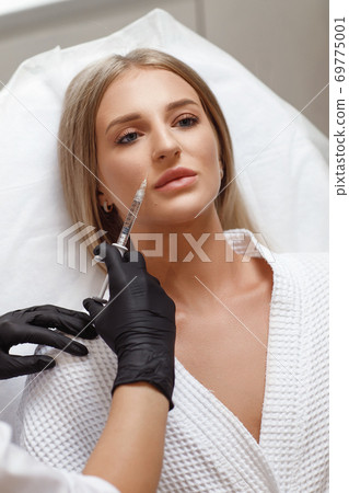 Enlarging lips, lip correction. Portrait white woman during an operation filling face wrinkles. 69775001