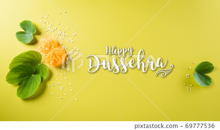 Happy Dussehra background concept. Green leaf and rice on yellow pastel background. Dussehra Indian Festival concept. 69777536