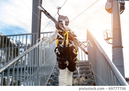 Portrait of young adult female brave skier tourist with skiing equipment enjoy having fun going to ride extreme suspended zipline wire flying over gorge canyon in mountains on background. Adrenaline Portrait of young adult female brave skier tourist with skiing equipment enjoy having fun going to ride extreme suspended zipline wire flying over gorge canyon in mountains on background. Adrenaline 69777706