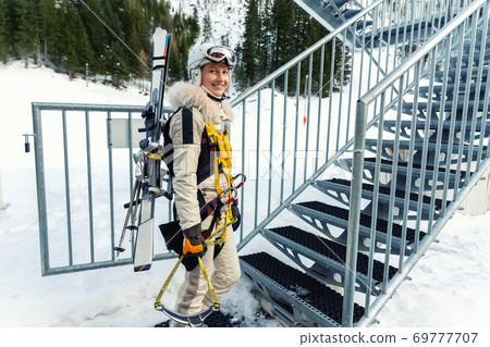 Portrait of young adult female brave skier tourist with skiing equipment enjoy having fun going to ride extreme suspended zipline wire flying over gorge canyon in mountains on background. Adrenaline Portrait of young adult female brave skier tourist with skiing equipment enjoy having fun going to ride extreme suspended zipline wire flying over gorge canyon in mountains on background. Adrenaline 69777707