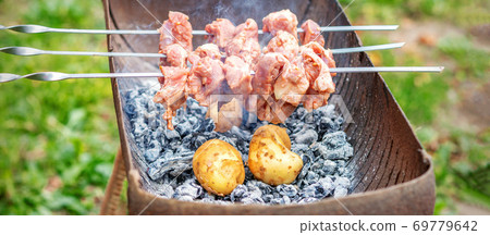 Man prepares barbecue meat with potatoes 69779642